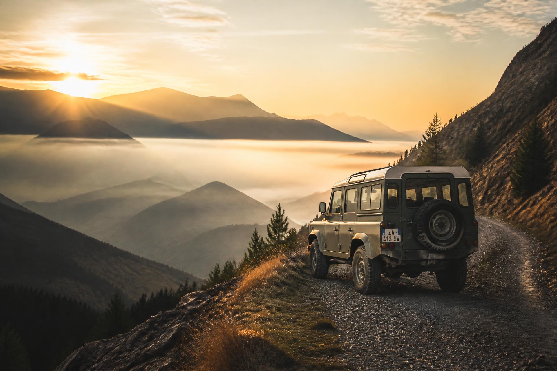 Vintage Land Rover Defender on a misty mountain road at sunrise
